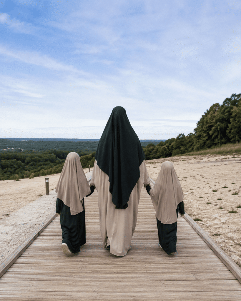 une femme musulmane voilée qui porte un khimar et une abaya de la marque Chic and mastour avec ses 2 filles qui portent également la même tenue sur le bord de la plage